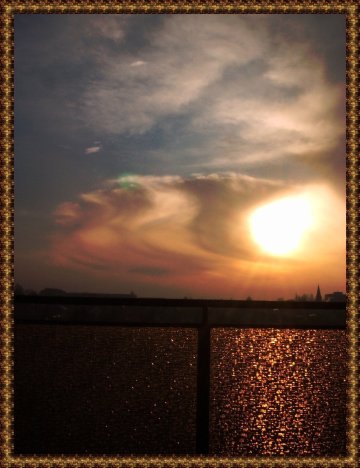 Felhők mögül átszűrődő Nap képe, előtte katedrálüveges erkélykorlát.